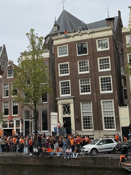 A vibrant crowd, many dressed in orange, gathers along the Herengracht in Centrum, Amsterdam, celebrating by the canal